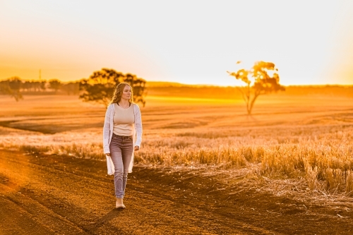 Teenage girl walking on dirt road against sunset rural landscape - Australian Stock Image