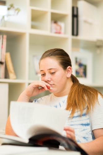 Teenage student reading a book for homework - Australian Stock Image