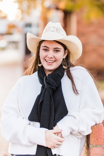 Teenager in scarf and hat leaning on wall smiling - Australian Stock Image