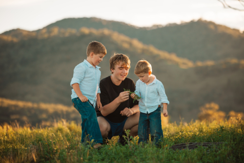 Teenager interacting with little boys on hilltop - Australian Stock Image