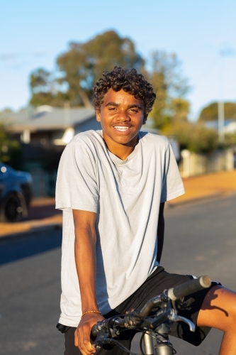 Teenager smiling looking at camera while resting on bicycle - Australian Stock Image