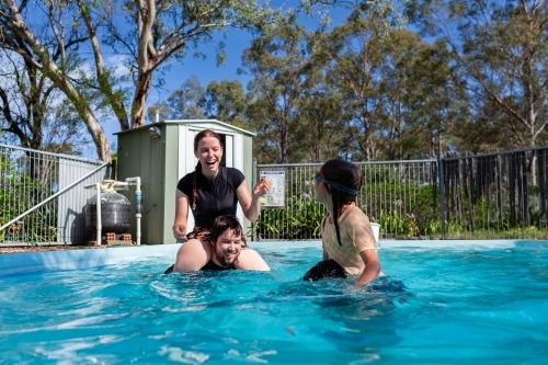 Teenagers and young adults playing shoulder wars in backyard swimming pool - Australian Stock Image