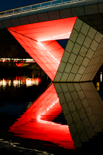 The Adelaide Riverbank Precinct Bridge crossing the River Torrens with bright red lights reflected - Australian Stock Image
