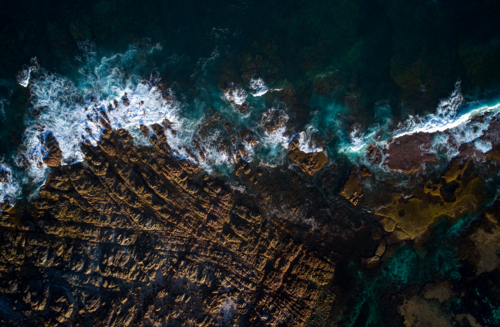 The dark ocean is kept at bay by jagged, exposed rock - Australian Stock Image