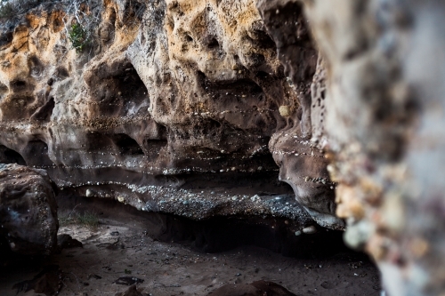 The entrance of a small, dark sandstone cave covered in a variety of tiny naturally embedded pebbles - Australian Stock Image