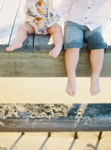 The legs of a young boy and baby hanging of the edge of a wharf - Australian Stock Image