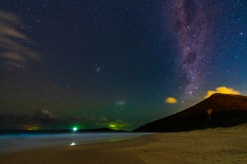 The Milky Way galaxy in the night sky over a coastal mountain at the end of a beach