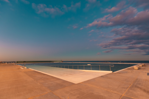 The Newcastle Ocean Baths at dusk with pink and purple fairy floss sky - Australian Stock Image