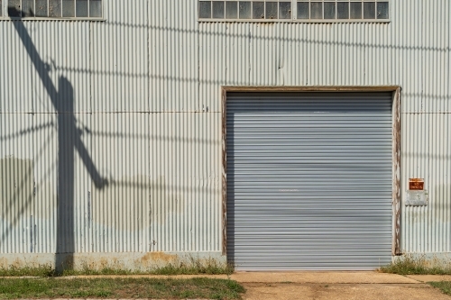 The shadow of a power pole cast onto a factory wall along side a roller door - Australian Stock Image