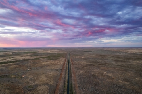 The sky is filled with pink storm clouds over a remote road with dirt tracks - Australian Stock Image