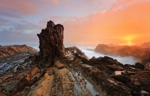 The sun rises over the ocean from rocky coastline in Australia - Australian Stock Image