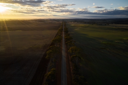 The sun rising over a farming landscape, with a bitumen road cutting through farmland in rural WA.