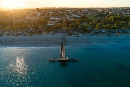 The sun rising over the horizon behind water and jetty at Coogee Beach in Western Australia. - Australian Stock Image