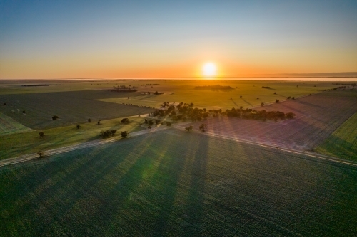The sun rising over the horizon looking down on paddocks and trees streaming sun rays. - Australian Stock Image