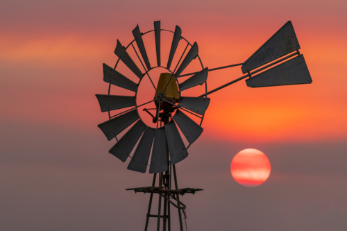 The Sun setting in an orange smoke cloud alongside a farm windmill - Australian Stock Image