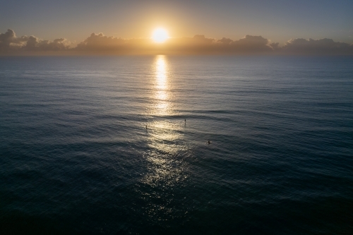 The sunrise over the ocean with paddle boarders waiting for waves - Australian Stock Image