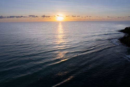 The sunrise over the ocean with surfers and paddle boarders waiting for the waves off the coast. - Australian Stock Image