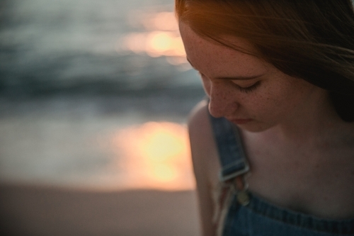 Thoughtful teenage girl on the beach at sunset wearing overalls - Australian Stock Image