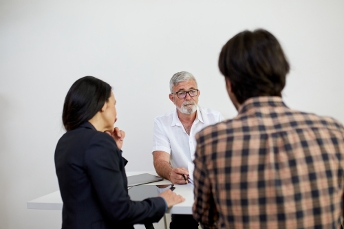 Three business people sitting at a desk, talking in a studio - Australian Stock Image