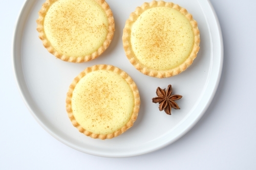 Three custard tarts on plate with star anise - Australian Stock Image