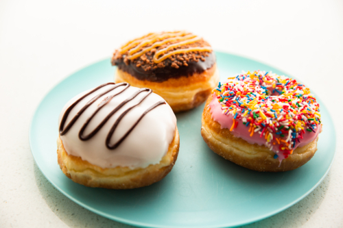 three doughnuts with different flavours and toppings on a blue plate - Australian Stock Image