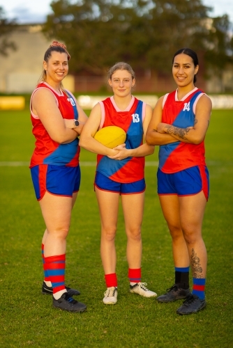 three female footballers standing on oval with arms crossed - Australian Stock Image