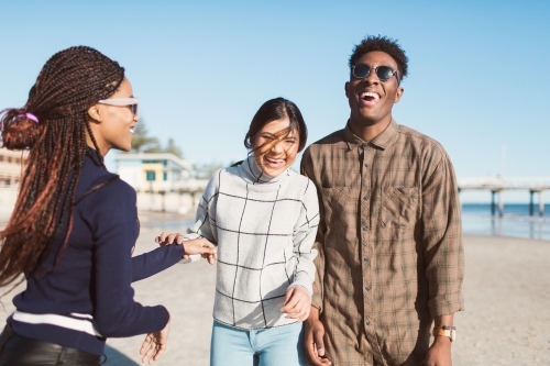 Three friends laughing together on the beach - Australian Stock Image