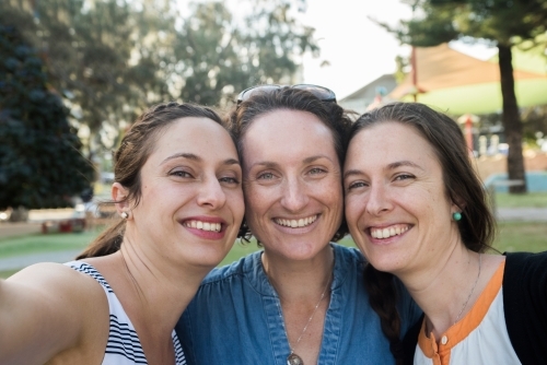 Three friends taking a selfie while smiling at the camera in a park. - Australian Stock Image