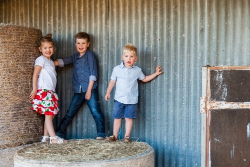 Three happy children on hay bales at farm - Australian Stock Image