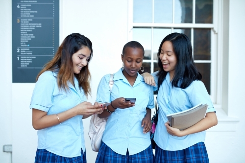 Three High School friends laughing whilst checking their mobile phones - Australian Stock Image