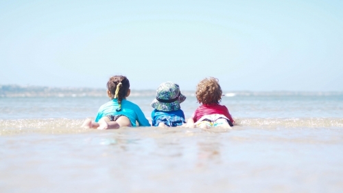 Three kids lying in the surf at the beach - Australian Stock Image