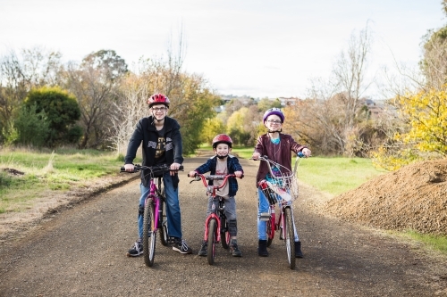 Three kids on their bikes on an unsealed road in park