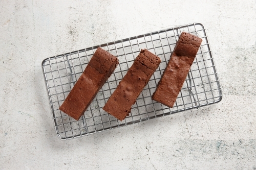 Three pieces of chocolate brownie on a baking rack - Australian Stock Image