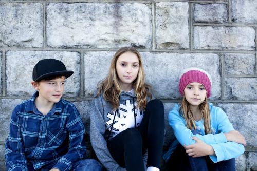 Three siblings sitting against a grey brick wall - Australian Stock Image