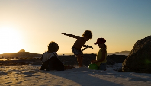 Three silhouette kids playing on the beach at sunset