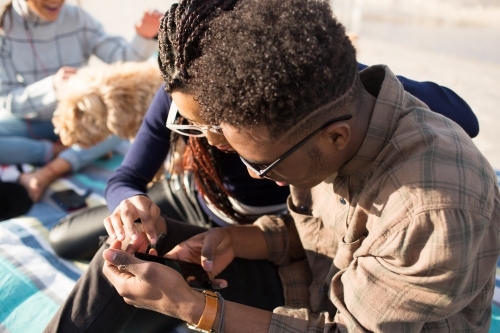 Three teenage friends sitting looking at a phone on a picnic rug - Australian Stock Image