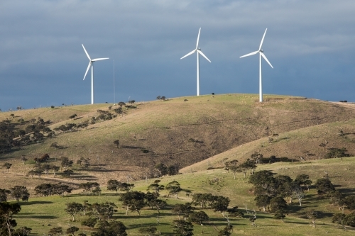 Three wind turbines on a grassy hill in a paddock - Australian Stock Image