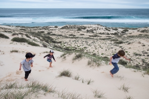 Three Young boys running through sand dunes on coast - Australian Stock Image