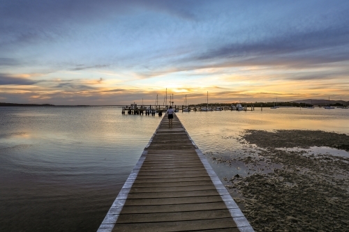 Timber jetty leading to sun setting over ocean - Australian Stock Image