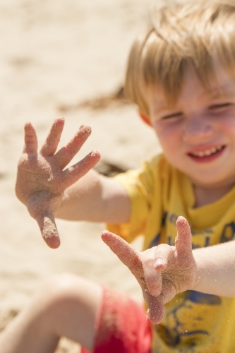 Toddler boy holding out sandy fingers at the beach