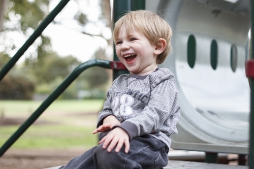 Toddler boy laughing at top of playground equipment