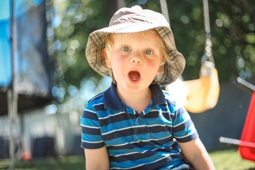 Toddler boy making surprised face wearing sun hat playing in backyard at home - Australian Stock Image