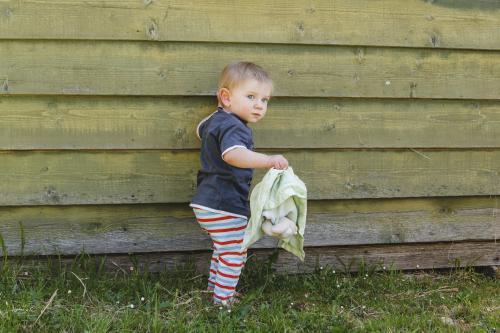 Toddler boy outside with his teddy beside green slat wall - Australian Stock Image