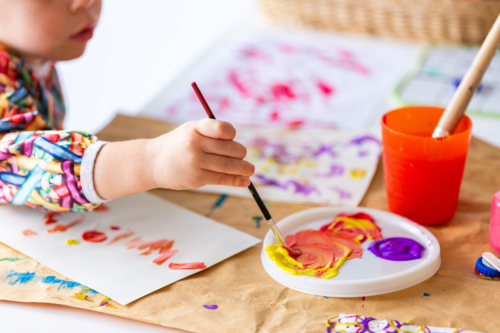 Toddler child at home painting with coloured paint on paper - Australian Stock Image