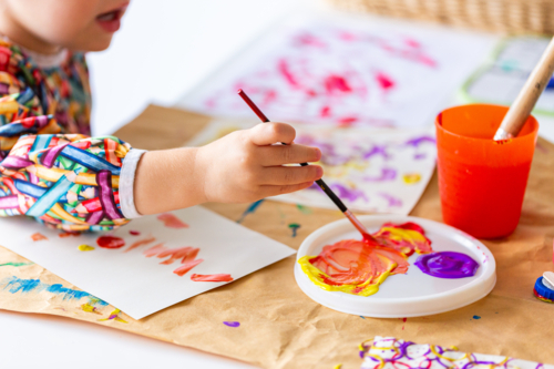 Toddler girl at home painting with coloured paint on paper - Australian Stock Image