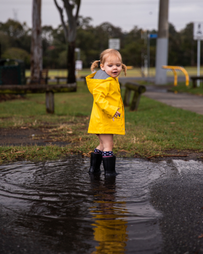 toddler in a yellow raincoat standing in a puddle - Australian Stock Image