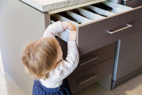 Toddler opening kitchen draw to get out spoon - Australian Stock Image