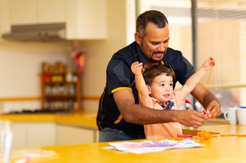 toddler playing with his dad in the kitchen - Australian Stock Image