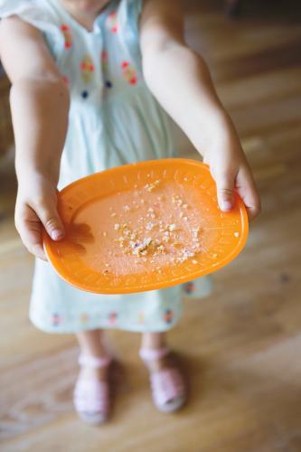 toddler showing empty plate after finishing lunch or snack - Australian Stock Image