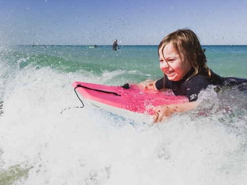 Toddler surfing a wave on a pink boogey board - Australian Stock Image